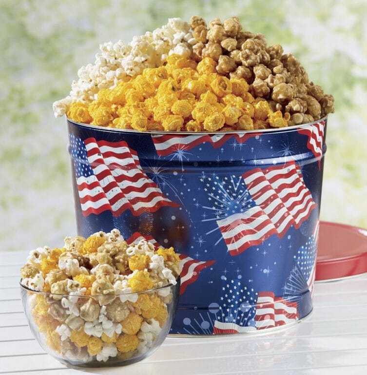 Patriotic popcorn tin filled with butter, cheese and caramel popcorn, and a clear bowl filled with mixed popcorn.